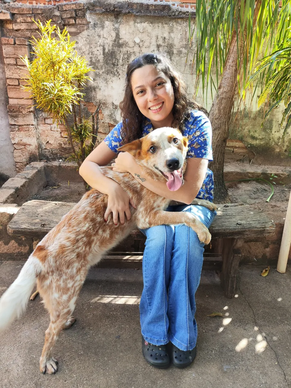 Dra. Vanessa sorrindo, abraçada a um cachorro no jardim